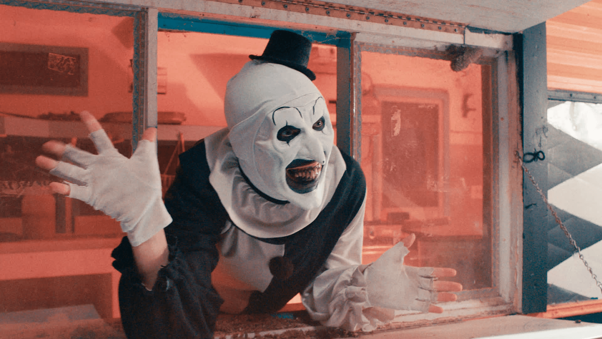 A picture of Art the Clown from Terrifier 2. He has white and black clown makeup, rotted teeth, and an unnaturally pointy face. He's leaning out of a food service window, grinning, and doing jazz hands.
